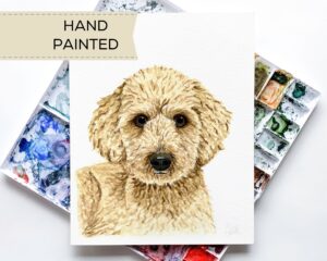 A custom watercolor pet portrait by Colle Creative featuring a Goldendoodle sitting on top of a paint palette