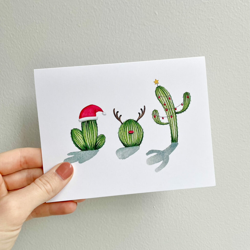 A hand holding up a Christmas Cacti card.