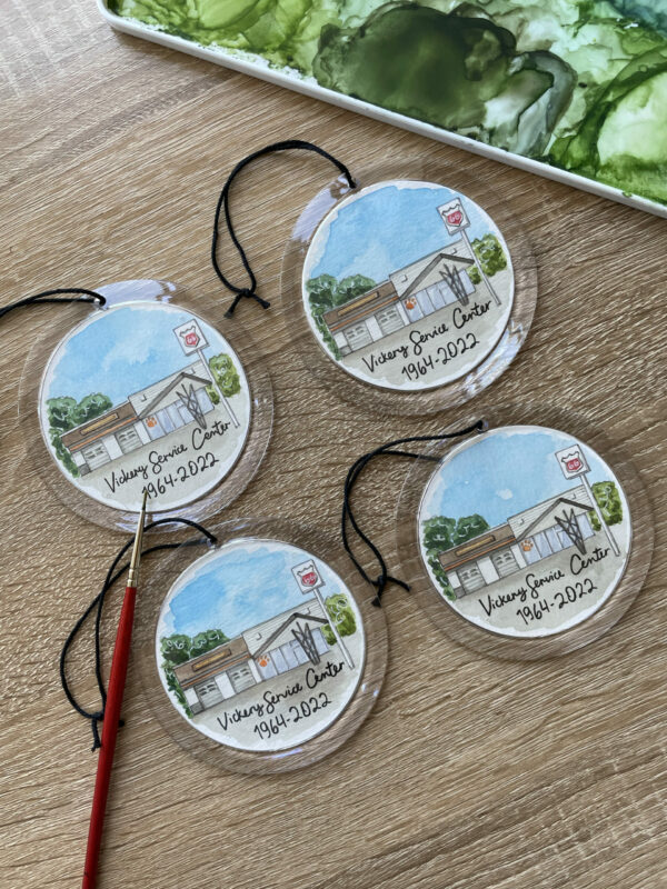 A set of four clear round ornaments with hand painted watercolor paintings of a gas station inside of them.